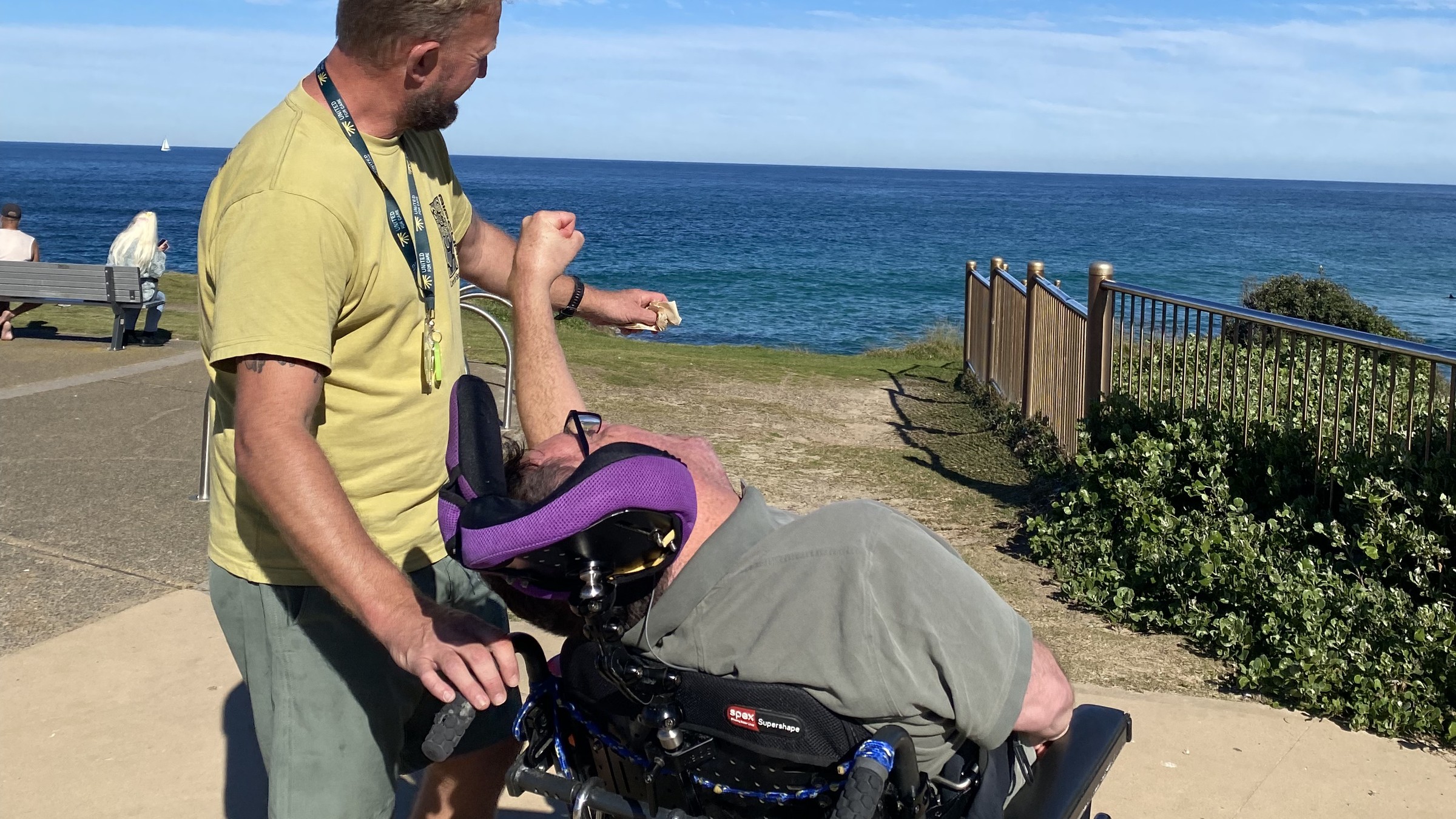 A member and their support worker walking together along the beach.