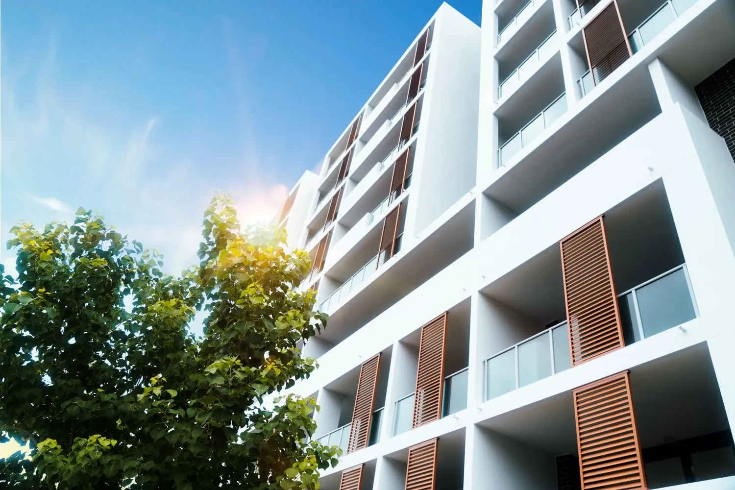 Looking up at a modern apartment building with timber screens and balconies against a clear blue sky in Liverpool.