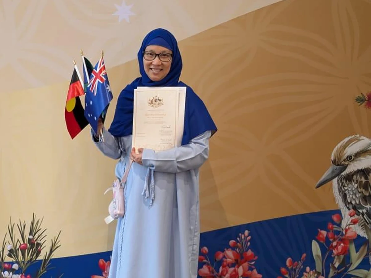 Mahasin holding her Australian citizenship certificate and small flags, dressed in blue at her ceremony.