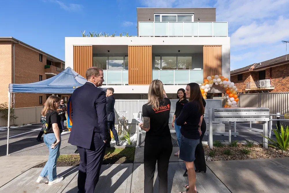 People gathered on the footpath outside the new Merrylands village home on opening day, with a balloon arch at the entry.
