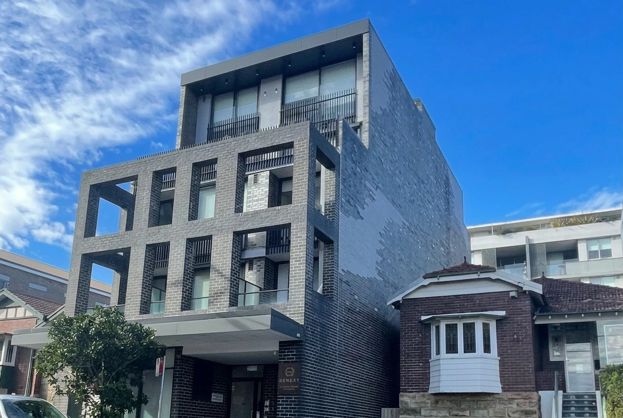 the Petersham village building, a four storey grey brick apartment building with balconies and a covered entry